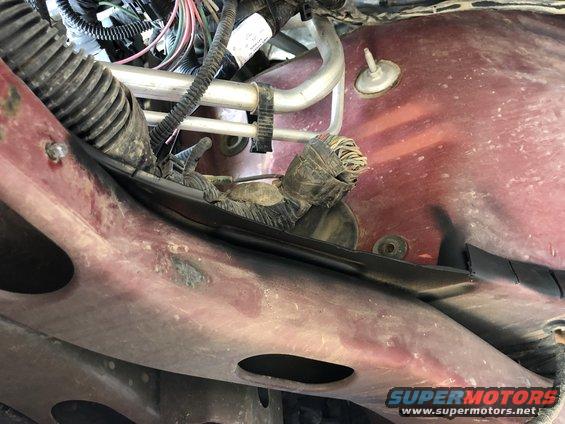 Close-up of a red vehicle's wiring harness and metal frame with a Supermotors.net watermark