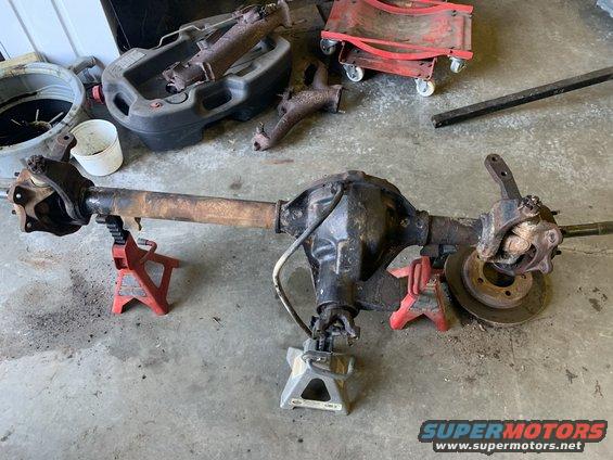 Jeep Dana 44 rear axle assembly on jack stands, with exhaust parts and oil drain pan nearby
