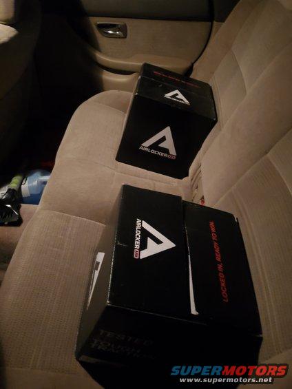 Two black boxes with AIRLOCKER logo and text 'LOCKED IN, READY TO WIN' on a vehicle seat