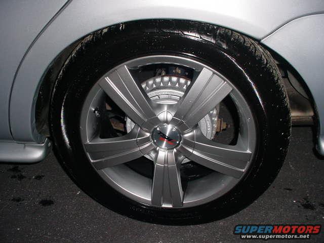 Silver car wheel with five spokes and a black tire. Brake caliper visible behind the wheel