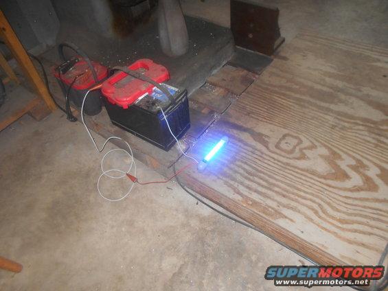 Two car batteries connected to a glowing blue light tube.