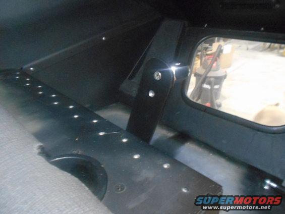 Interior view of a vehicle with a grey seat and black paneling with visible rivets. A window shows a vacuum cleaner