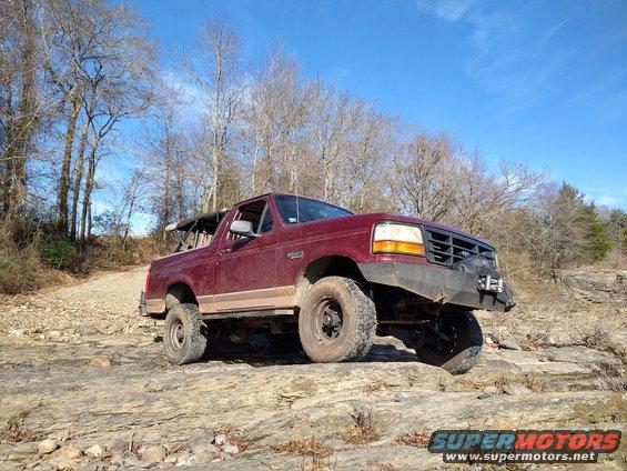 1996 Ford Bronco with aftermarket bumper and winch driving over rocks