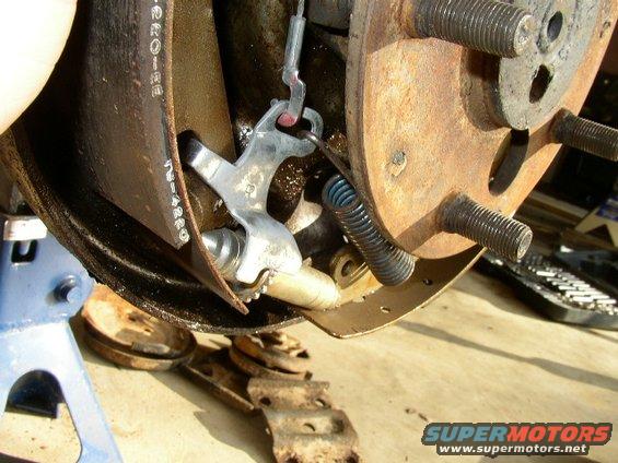 Close-up of a rusty brake drum assembly with a hand visible, showing brake shoes and springs