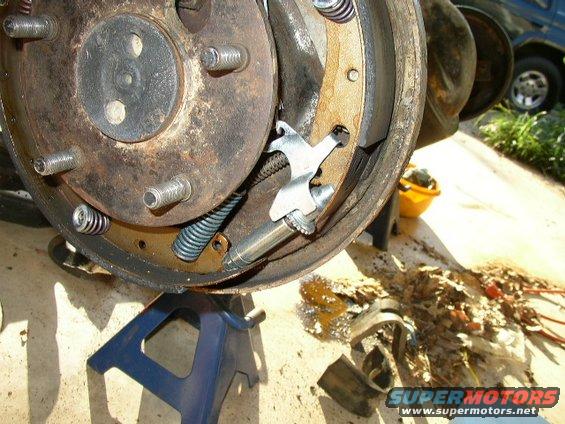 close-up of a vehicle's drum brake assembly on a jack stand, with a dark SUV visible in the background