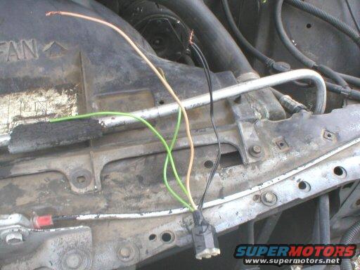 Engine bay with exposed wires and a metal bracket. Text "FAN" is visible on a black plastic shroud