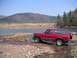1994 Ford Bronco - A red 1994 Ford Bronco is parked near the water's edge with a wooded hill in the background.