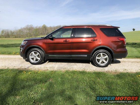 Orange 2016 Ford Explorer SUV parked on a gravel road with grass and trees in the background
