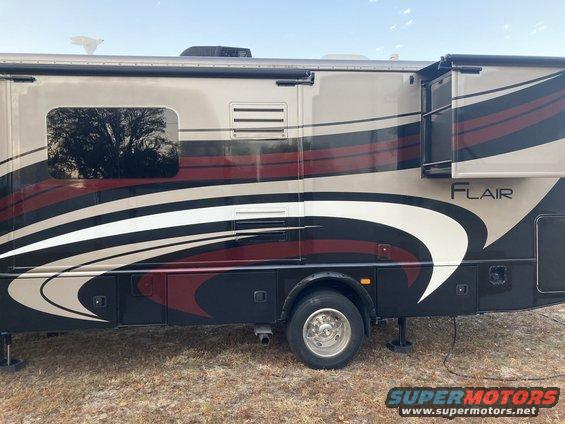 Side view of a recreational vehicle with "FLAIR" badging. It has a beige and maroon stripe design