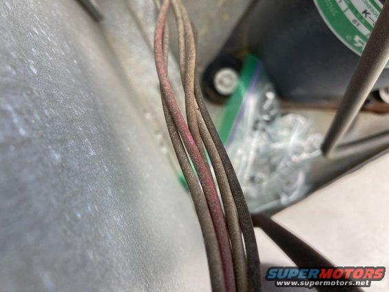 Close-up of several electrical wires, some with pink markings, near a motor and a plastic bag