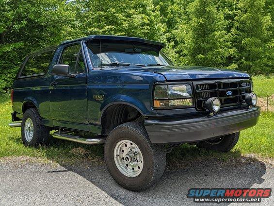 Dark blue Ford Bronco parked on a gravel and grass area with trees in the background