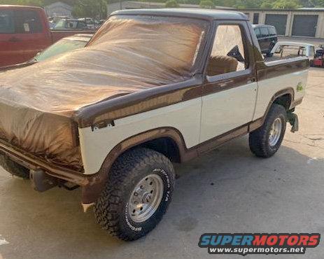 1984 Ford Bronco covered in a brown tarp, parked outdoors