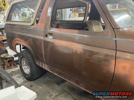 Side view of a brown 1984 Ford Bronco with primer showing, in a garage