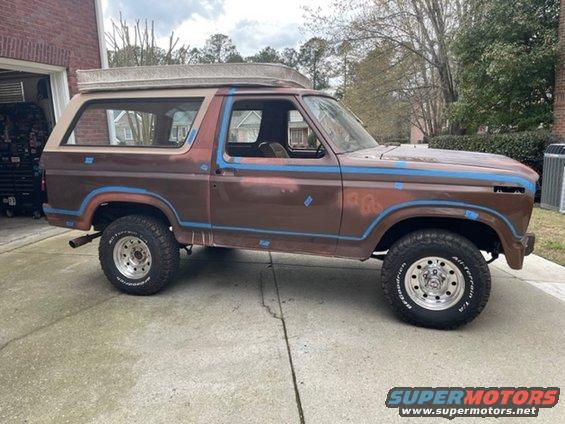 Brown Ford Bronco with blue trim, showing primer spots and a mattress on the roof