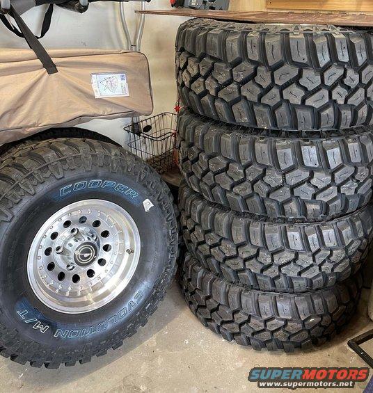 Stack of four off-road tires and one Cooper Evolution M/T tire with a polished aluminum wheel