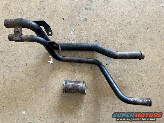 Two rusty black metal pipes and a silver metal sleeve on a concrete surface