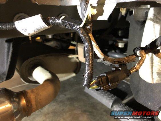Close-up of a vehicle's exhaust pipe and wiring harness with a black connector