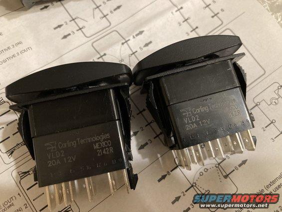 Two black Carling Technologies VLD2 20A 12V switches with metal pins, resting on a diagram