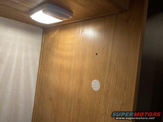 Interior cabinet with overhead LED light and two small holes drilled into wood paneling. Supermotors.net logo visible at bottom right
