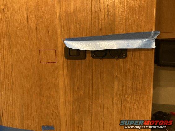 Wood-grain interior panel with two electrical outlets and masking tape
