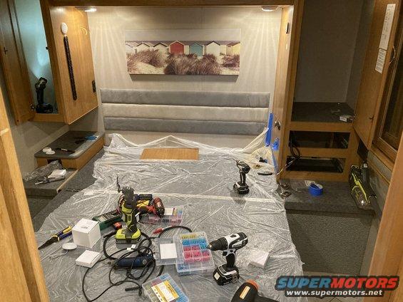 RV interior with bed covered in plastic, tools, and wiring supplies