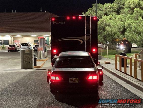 Car being towed by an RV at a gas station at night. License plate reads EEJ 1024