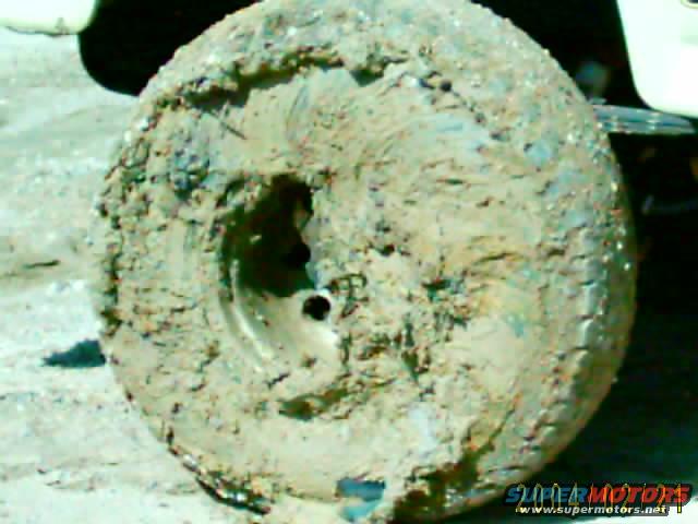Mud-covered tire and wheel, with part of a white vehicle visible