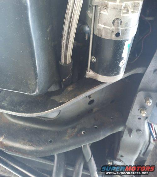 Underside of a vehicle showing braided metal transmission cooler lines connected to a black and silver component, possibly an air compressor