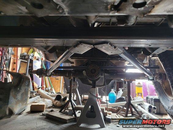Underside of a vehicle on jack stands, showing custom suspension links and a differential