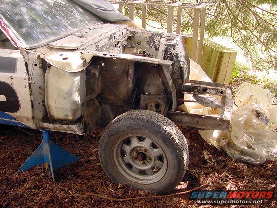 1969 Ford Mustang chassis on jack stands, front view, white body with racing numbers, heavily weathered