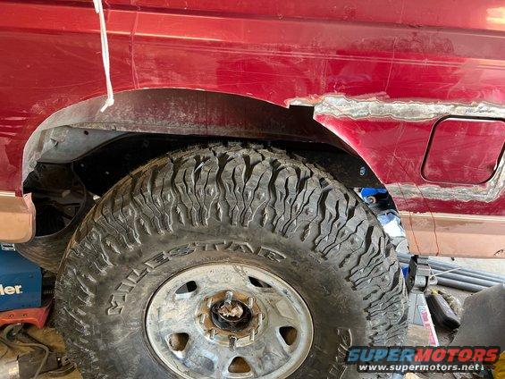 Red SUV's rear fender area with a large off-road tire. Bodywork is being done on the fender