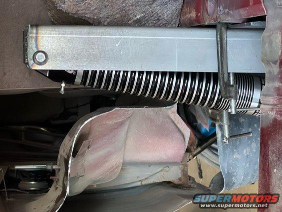 Aftermarket shock absorber with black protective boot clamped to vehicle frame