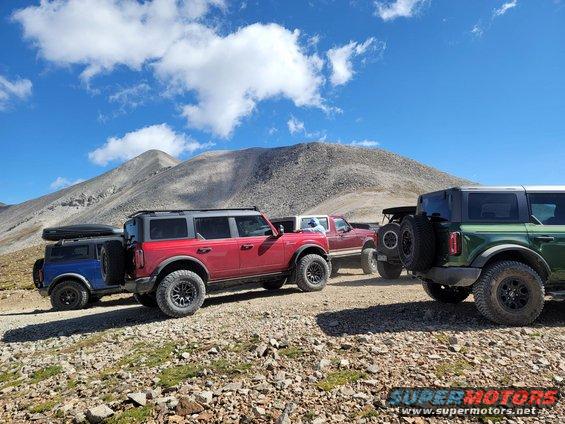 Red Ford Bronco towing a blue Bronco with a cargo box, parked on a rocky mountain road