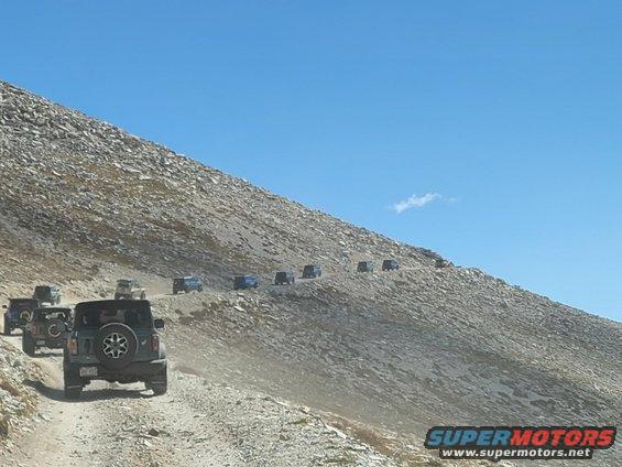 Several Jeeps driving up a rocky mountain road under a clear blue sky