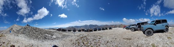 Blue Ford Bronco parked on a rocky mountain summit with other SUVs