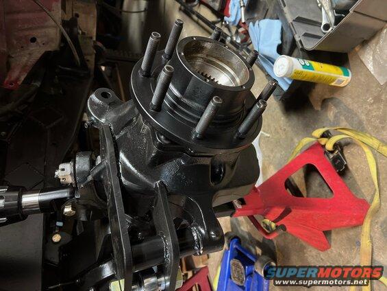 Front wheel hub assembly with five studs, black painted metal, on a workbench with jack stands