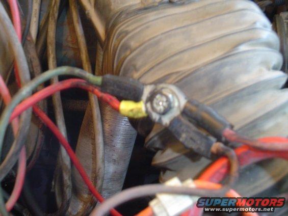 Close-up of engine wiring with red and green wires connected to a terminal, with a ribbed hose in the background