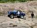 1973 Ford Bronco - A blue Ford Bronco navigates a rocky terrain with several passengers.