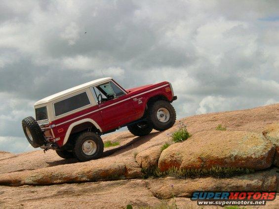 Red and white Ford Bronco climbing a rocky hill, with a spare tire mounted on the rear