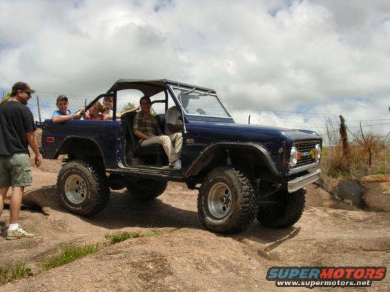Blue 1973 Ford Bronco driving on rocks with passengers