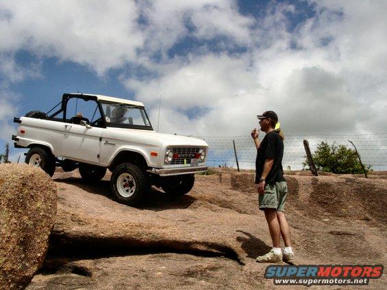 1973 Ford Bronco parked on large rocks with a man standing nearby