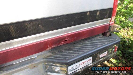 Red and silver truck rear bumper with rust damage and two stickers