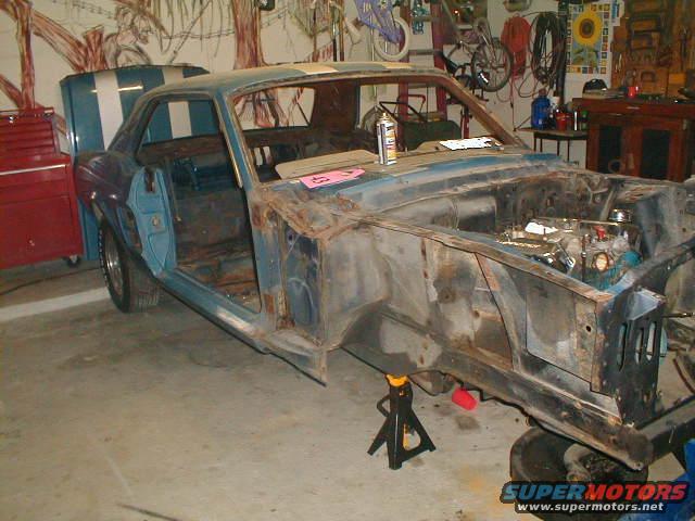 1967 Ford Mustang body in garage, stripped down and on jack stands, engine partially visible