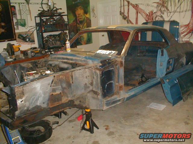 Blue classic car body in a garage, missing engine and front clip. Doors are open