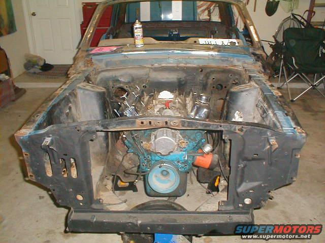 1967 Ford Mustang engine bay with blue engine, rust, and missing parts