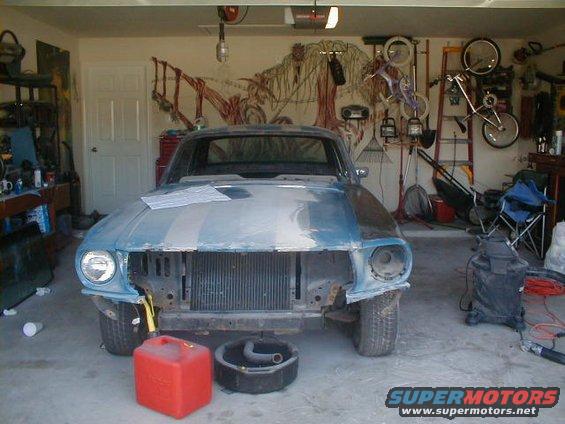 1967 Ford Mustang in a garage, undergoing restoration, with its front end disassembled