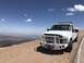 2008 Ford F-250 - A white pickup truck is parked on a dirt road overlooking a desert landscape under a clear blue sky.