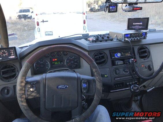 Interior of a truck cab, showing steering wheel, dashboard, CB radio, and Garmin GPS. Another truck is visible outside