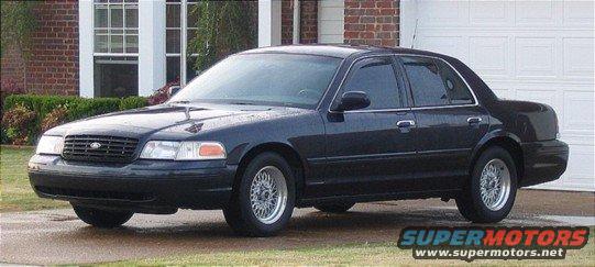 Dark sedan parked in front of a brick house and garage. It has a black grille and chrome door handles