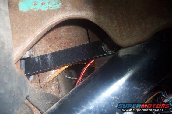 Close-up of rusty metal with a black bracket and red wire. Text on a turquoise tag reads '42 32 C'